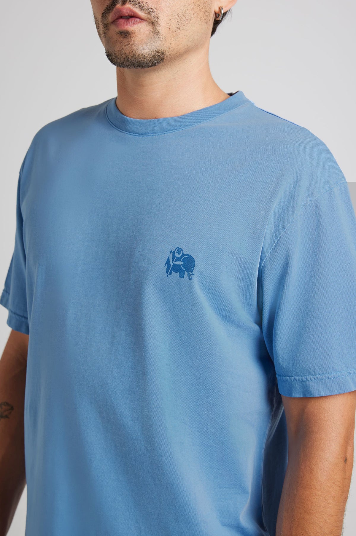 Close-up of a person wearing a blue short-sleeved T-shirt with a small chest graphic | TP_IMAGE_TYPE=DETAIL