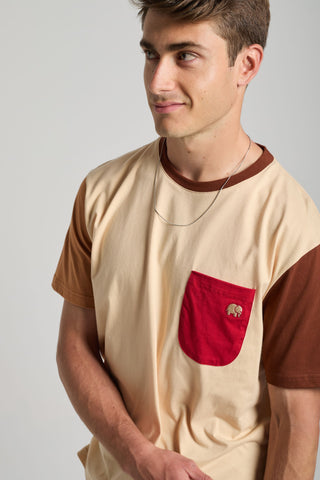 Personne portant un t-shirt color block gris sable avec une manche marron et une poche rouge, arborant un motif d'éléphant ludique | TP_IMAGE_TYPE=MODEL_FRONT
