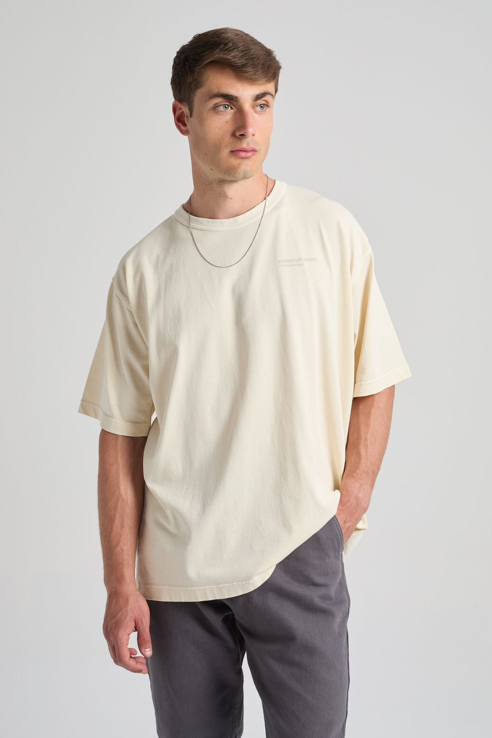 Persona che indossa una T-shirt core oversize in bianco panna, abbinata a pantaloni casual, in piedi su uno sfondo neutro | TP_IMAGE_TYPE=MODEL_FRONT