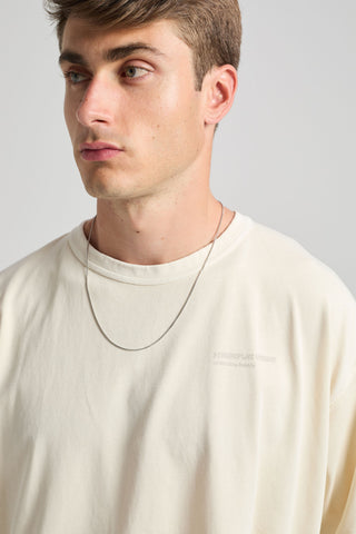 Persona che indossa una T-shirt Core Oversized in Off White con un discreto logo in rilievo, abbinata a una collana semplice, in uno scatto in stile ravvicinato. | TP_IMAGE_TYPE=MODEL_FRONT