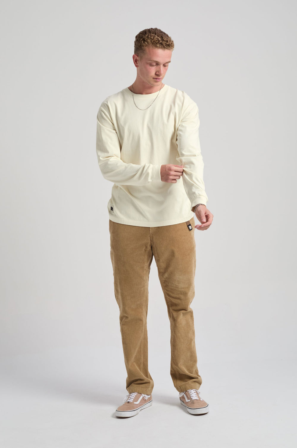 Persona che indossa una Flowers L/S T-Shirt in Antique White, abbinata a pantaloni in velluto a coste e scarpe casual, mentre si sistema la manica in piedi davanti a uno sfondo chiaro. | TP_IMAGE_TYPE=MODEL_FRONT