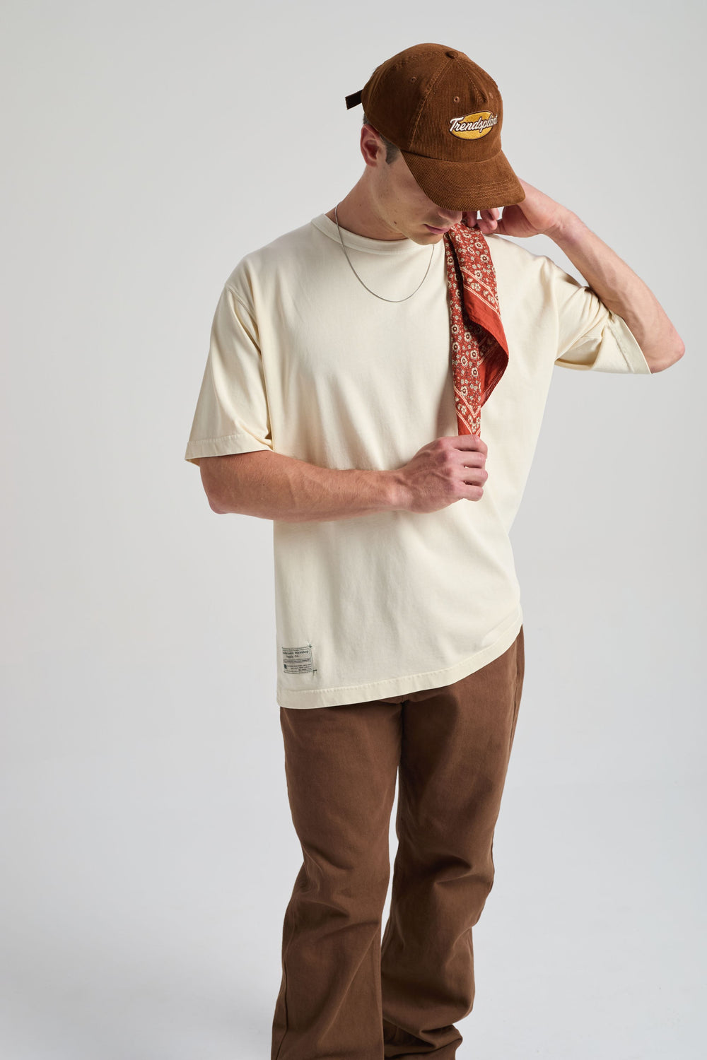 Personne portant un t-shirt oversize blanc antique, tenant un bandana à motifs, associé à un pantalon marron et une casquette marron | TP_IMAGE_TYPE=MODEL_FRONT