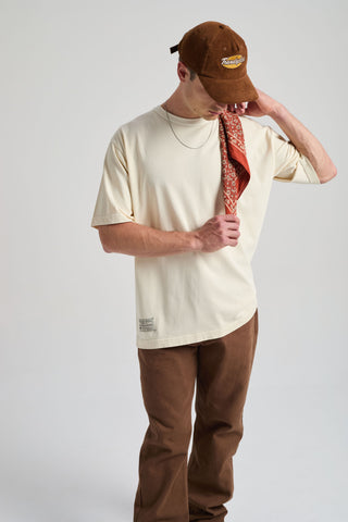 Personne portant un t-shirt oversize blanc antique, tenant un bandana à motifs, associé à un pantalon marron et une casquette marron | TP_IMAGE_TYPE=MODEL_FRONT