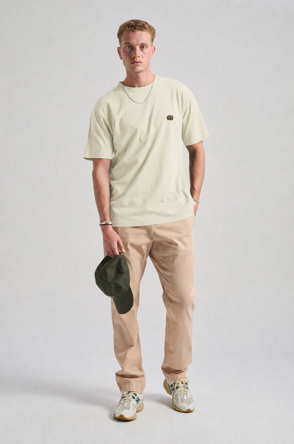 Persona che indossa una Spring T-Shirt in Antique White, abbinata a pantaloni chiari e con un cappellino verde in mano | TP_IMAGE_TYPE=MODEL_FRONT