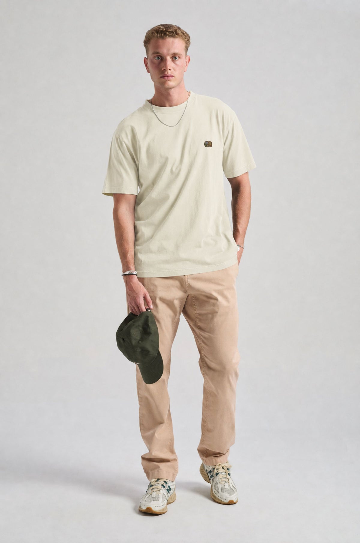 Persona che indossa una Spring T-Shirt in Antique White, abbinata a pantaloni chiari e con un cappellino verde in mano | TP_IMAGE_TYPE=MODEL_FRONT
