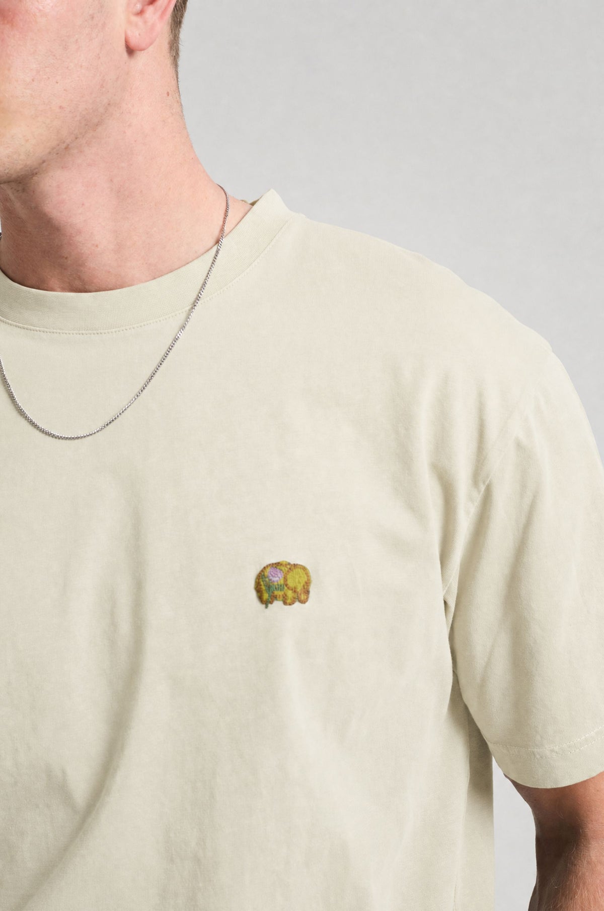 Persona che indossa una Spring T-Shirt in Antique White con un elefante ricamato sul petto. | TP_IMAGE_TYPE=MODEL_FRONT