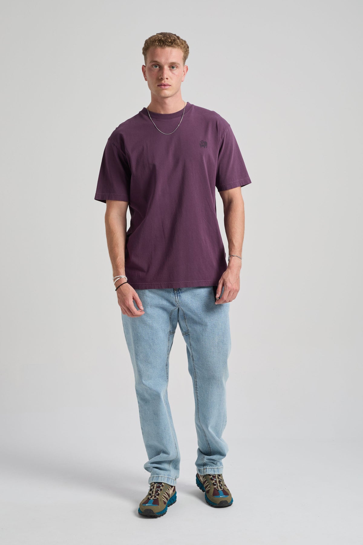Person wearing a Winter Bloom t-shirt in a deep purple shade, styled with light blue jeans and sneakers, standing against a neutral backdrop | TP_IMAGE_TYPE=MODEL_FRONT