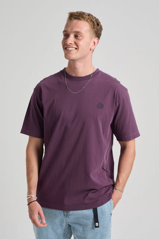 Person wearing the Bloom T-Shirt in Winter Bloom, a stylish purple shirt, paired with light blue jeans and a silver chain necklace, smiling confidently against a neutral background. | TP_IMAGE_TYPE=MODEL_FRONT