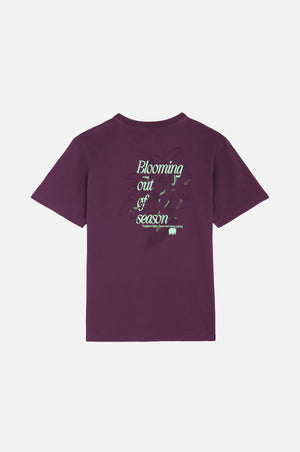 Person wearing Bloom T-Shirt Winter Bloom in a rich purple color, showcasing the back design with the text "Blooming out of season." | TP_IMAGE_TYPE=MODEL_BACK