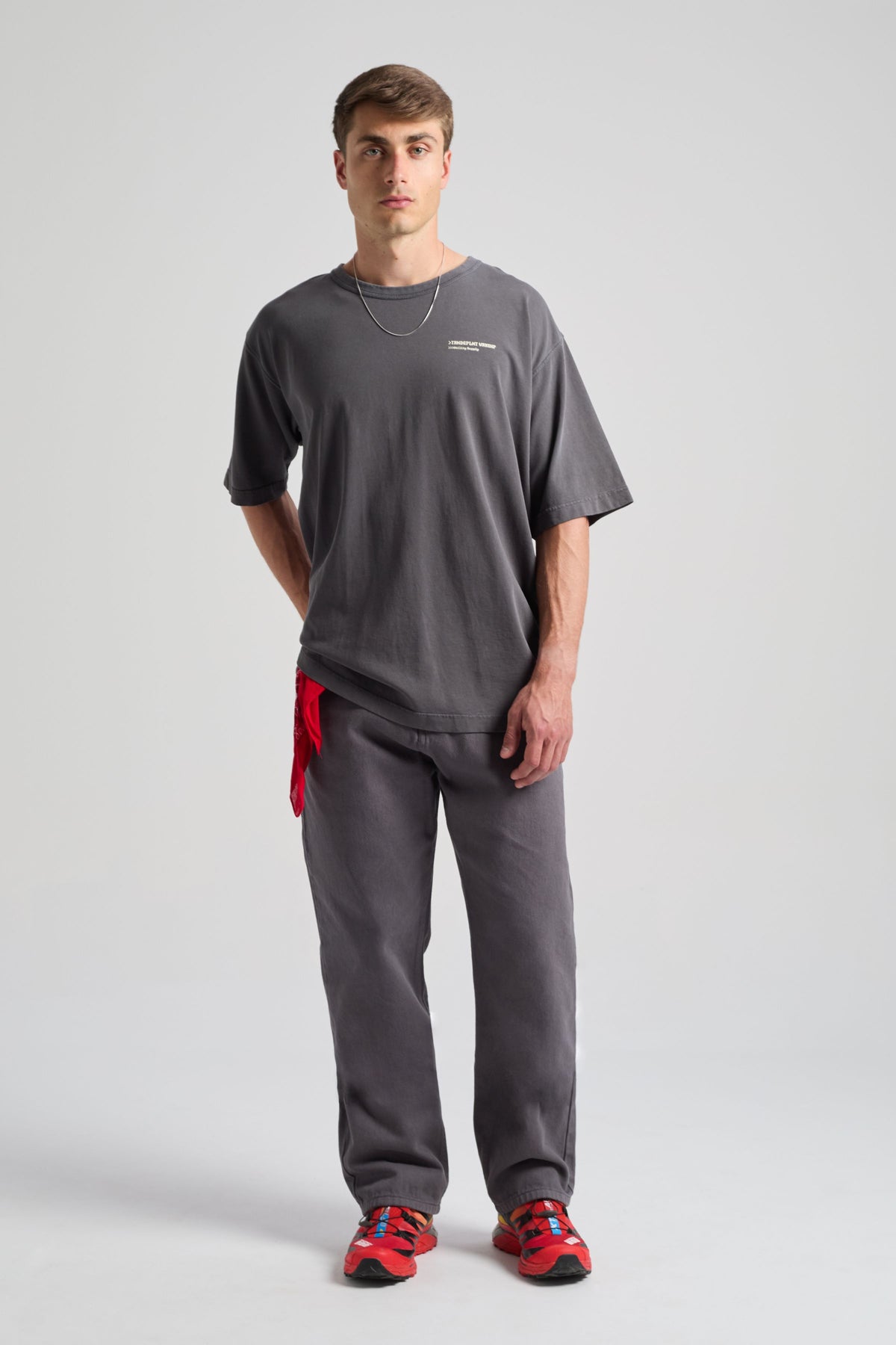 Persona che indossa una Core Oversized T-shirt in Forged Iron con vestibilità rilassata, abbinata a pantaloni coordinati e un accessorio rosso | TP_IMAGE_TYPE=MODEL_FRONT