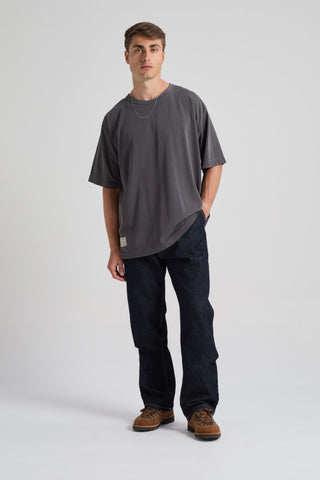 Persona che indossa una t-shirt oversize Forged Iron con maniche arrotolate, abbinata a jeans scuri e sneakers, in posa in uno studio. | TP_IMAGE_TYPE=MODEL_FRONT