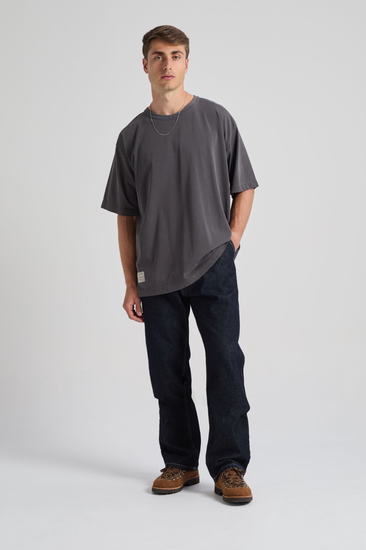 Persona che indossa una t-shirt oversize Forged Iron con maniche arrotolate, abbinata a jeans scuri e sneakers, in posa in uno studio. | TP_IMAGE_TYPE=MODEL_FRONT
