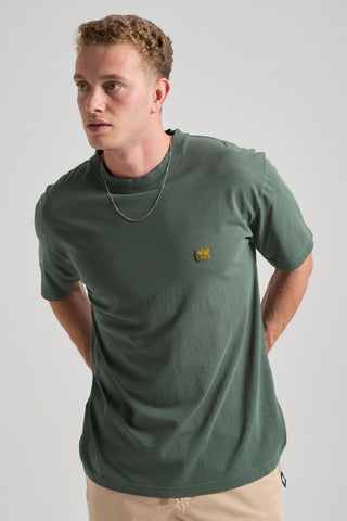 Persona che indossa una t-shirt verde con un piccolo logo su uno sfondo neutro. TP_IMAGE_TYPE=MODEL_FRONT