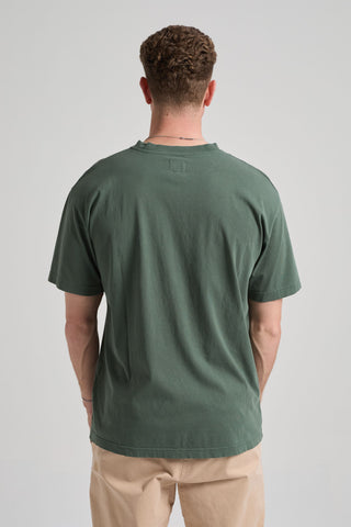 Persona che indossa una t-shirt verde e pantaloni beige su uno sfondo neutro. TP_IMAGE_TYPE=MODEL_BACK