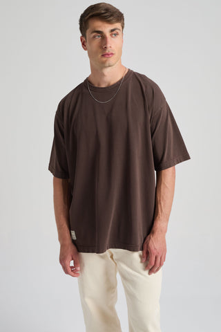 Persona che indossa la T-shirt Supply Oversized nel colore Coffee Bean, abbinata a pantaloni chiari, in piedi su uno sfondo neutro | TP_IMAGE_TYPE=MODEL_FRONT