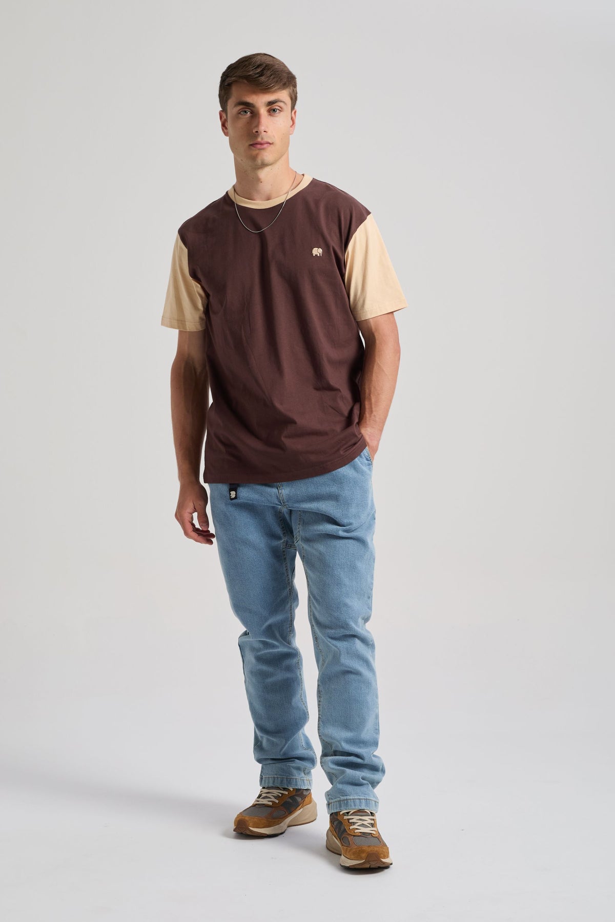 Person wearing a Color Block T-Shirt in Solemnity Brown with a contrasting light brown sleeve, paired with light blue jeans and sneakers | TP_IMAGE_TYPE=MODEL_FRONT