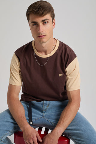 Person wearing a Color Block T-Shirt in Solemnity Brown with contrasting light brown sleeves, sitting on a red stool | TP_IMAGE_TYPE=MODEL_FRONT