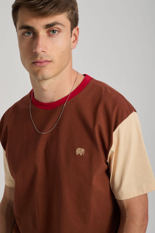 Person wearing a color block t-shirt in Cherry Mahogany and light beige with a red collar, featuring an embroidered elephant logo. | TP_IMAGE_TYPE=MODEL_FRONT