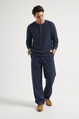 Persona che indossa una maglia henley a maniche lunghe blu navy e pantaloni della tuta blu navy abbinati, in piedi su uno sfondo da studio grigio chiaro. TP_IMAGE_TYPE=MODEL_FRONT