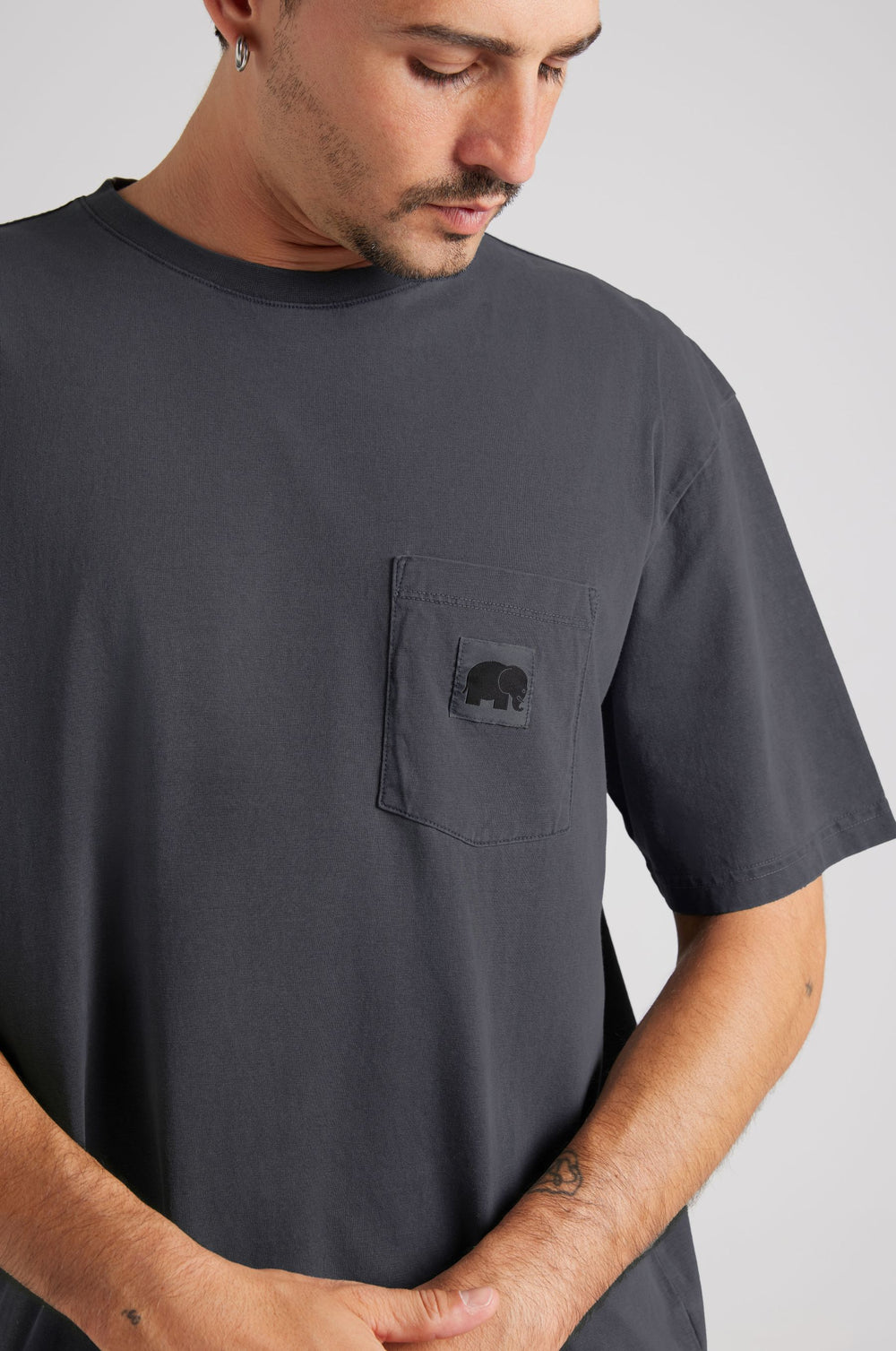 Persona che indossa una camicia Garza Magnet Grey con logo sulla tasca, che guarda verso il basso | TP_IMAGE_TYPE=MODEL_FRONT