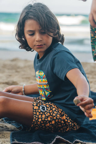 Personne portant un Kid's Organic Navajo Classic T-Shirt bleu, assise sur la plage | TP_IMAGE_TYPE=LIFESTYLE