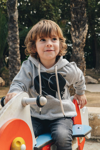 Persona che indossa una Kid's Organic Classic Hoodie Heather Grey seduta su un veicolo giocattolo | TP_IMAGE_TYPE=LIFESTYLE