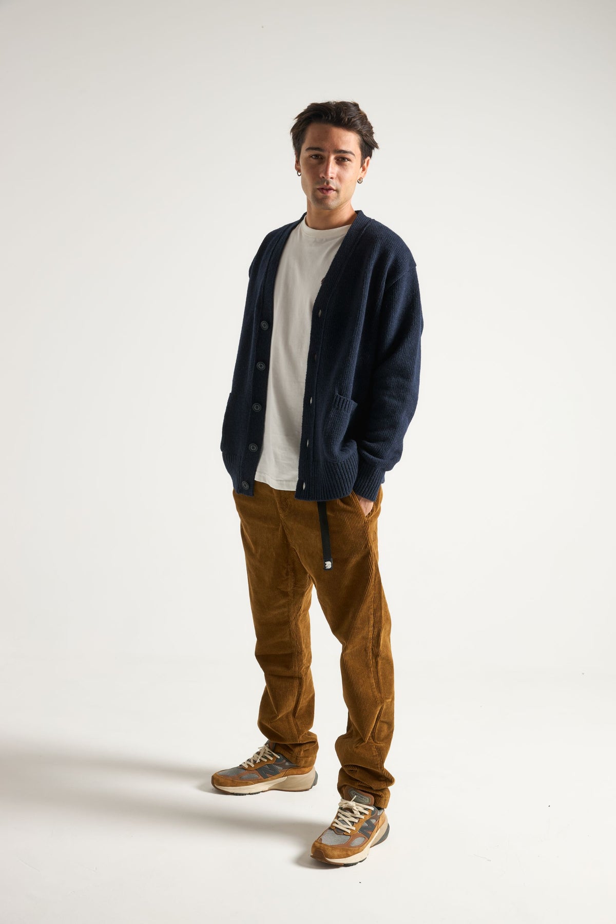 Personne portant un cardigan Relleu bleu marine foncé sur un t-shirt blanc, associé à un pantalon en velours côtelé marron et des baskets, en pose dans un studio. | TP_IMAGE_TYPE=MODEL_FRONT
