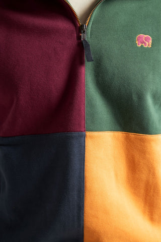 Persona che indossa una felpa color block con zip a metà dal titolo "Harlequin", con sezioni bordeaux, verde, blu navy e arancione, vista di fronte. | TP_IMAGE_TYPE=MODEL_FRONT