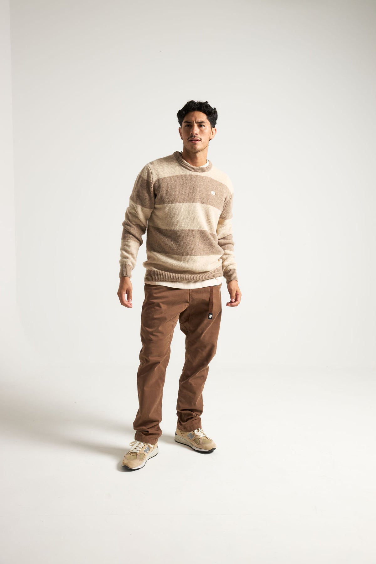 Persona che indossa il Sella Knit in Latte/Nomad Brown, abbinato a pantaloni e sneakers marroni coordinati, in posa in uno studio fotografico. | TP_IMAGE_TYPE=MODEL_FRONT
