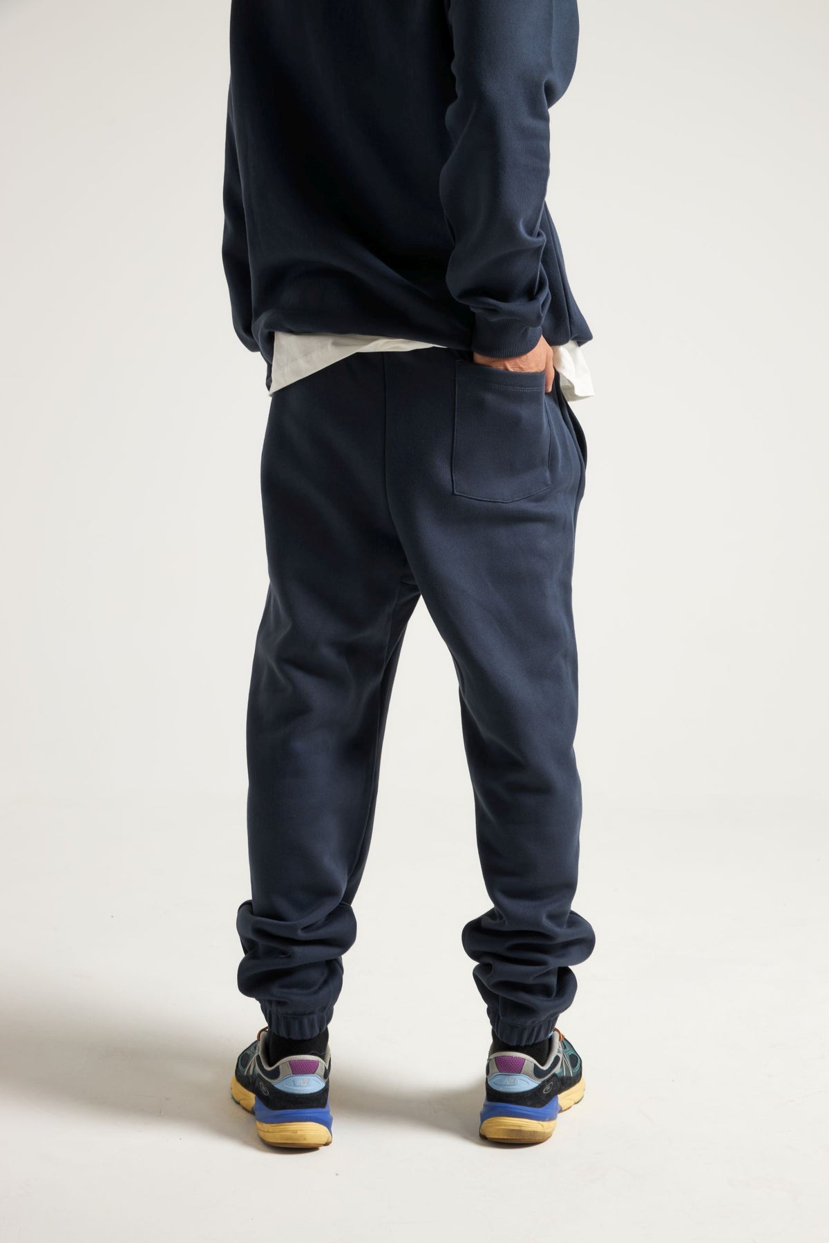 Persona che indossa Organic Essential Sweatpants in Trendsplant Blue, vista posteriore con le mani nelle tasche | TP_IMAGE_TYPE=MODEL_BACK