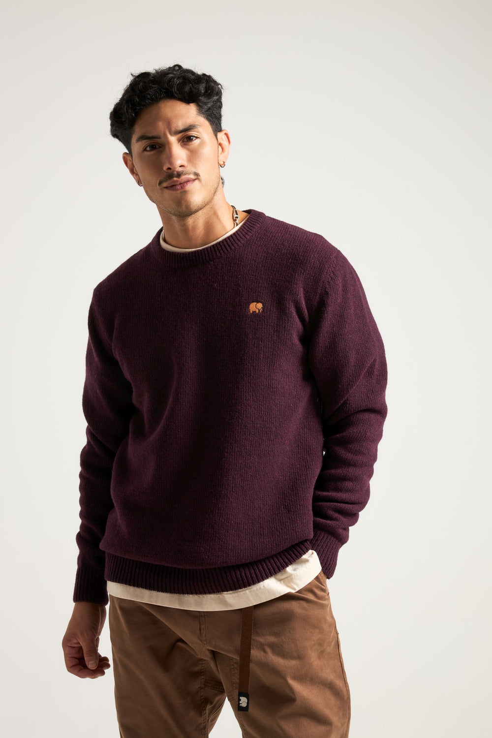 Persona che indossa un maglione Sella Knit rosso vino, in piedi con le mani in tasca e sfondo neutro | TP_IMAGE_TYPE=MODEL_FRONT