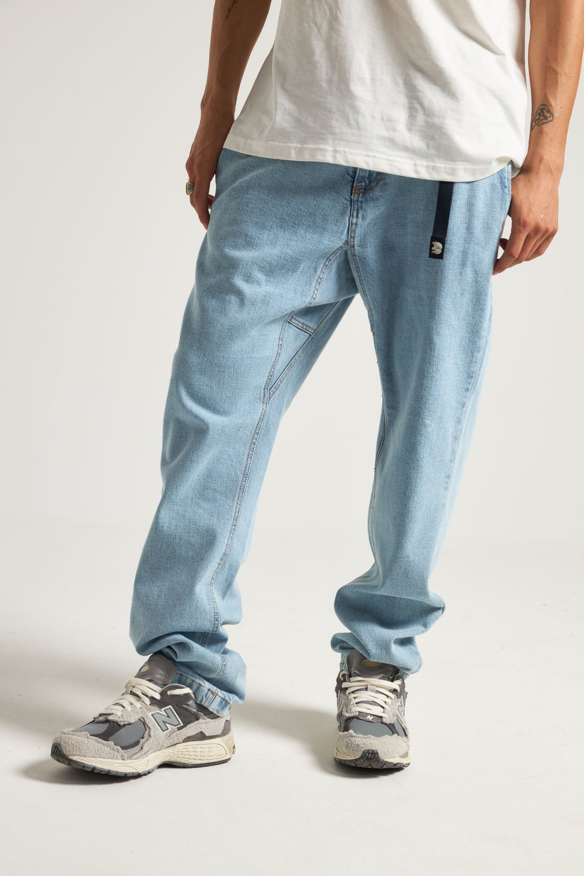 Personne portant le Recycled Denim Climber Pant Light Wash avec une chemise blanche décontractée et des baskets, illustrant une coupe décontractée et un style en denim délavé clair | TP_IMAGE_TYPE=MODEL_FRONT