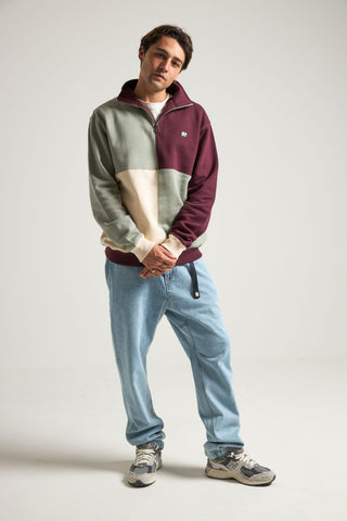 Persona che indossa una felpa Color Block con zip a un quarto in Iron Veil, con sfumature di verde, granata e crema, abbinata a pantaloni azzurro chiaro e sneakers. | TP_IMAGE_TYPE=MODEL_FRONT