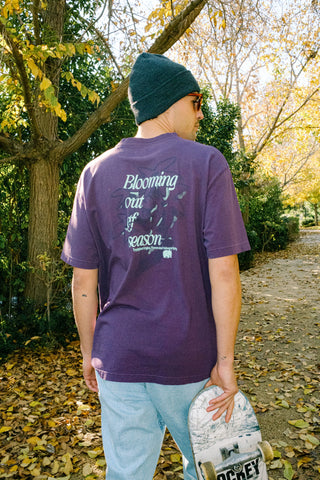 Person wearing the Bloom T-Shirt Winter Bloom in a vibrant shade of purple, showcasing the back design amidst an autumnal outdoor setting. | TP_IMAGE_TYPE=MODEL_BACK