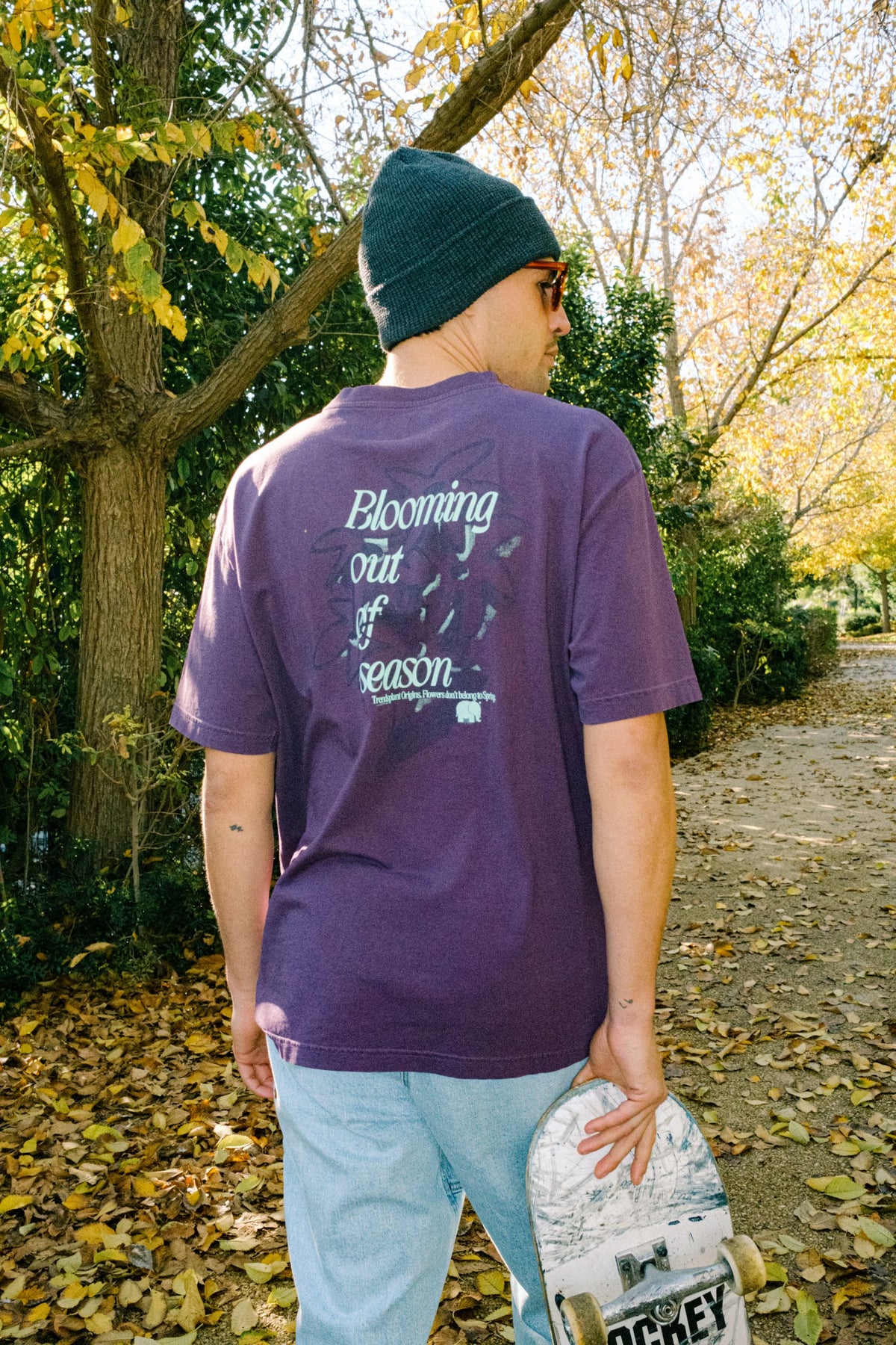 Person wearing the Bloom T-Shirt Winter Bloom in a vibrant shade of purple, showcasing the back design amidst an autumnal outdoor setting. | TP_IMAGE_TYPE=MODEL_BACK