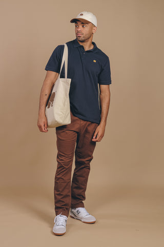 Personne portant une chemise polo Organic Essential Polo Shirt en bleu Trendsplant Blue, associée à un pantalon marron décontracté, debout avec assurance | TP_IMAGE_TYPE=MODEL_FRONT