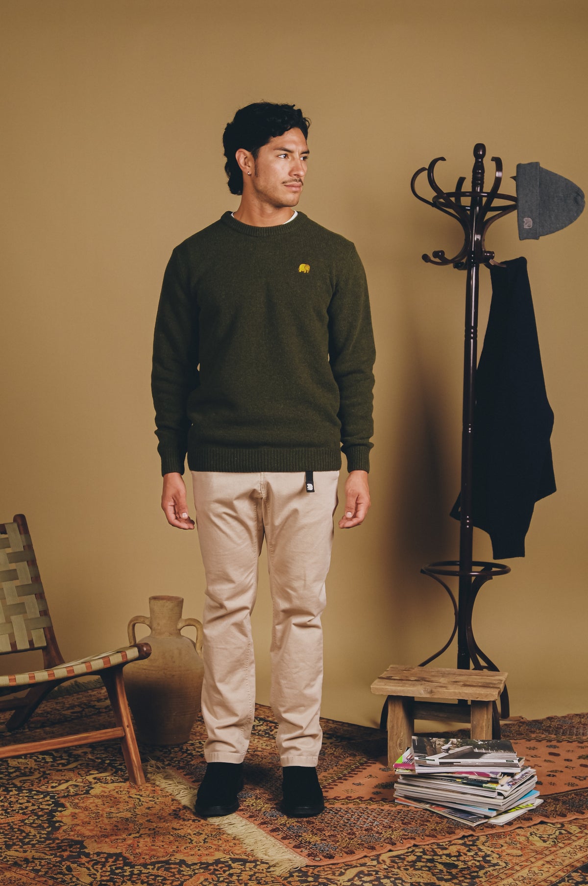 Persona che indossa una Sella Knit in Ivy Green, abbinata a pantaloni beige e scarpe nere, in un ambiente caldo e domestico. | TP_IMAGE_TYPE=MODEL_FRONT