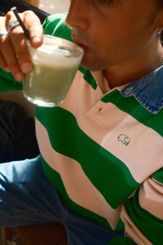 Personne portant un Yard Rugby Polo vert fougère et rose nuage avec un col en denim et un logo éléphant brodé, sirotant une boisson verte. | TP_IMAGE_TYPE=LIFESTYLE.