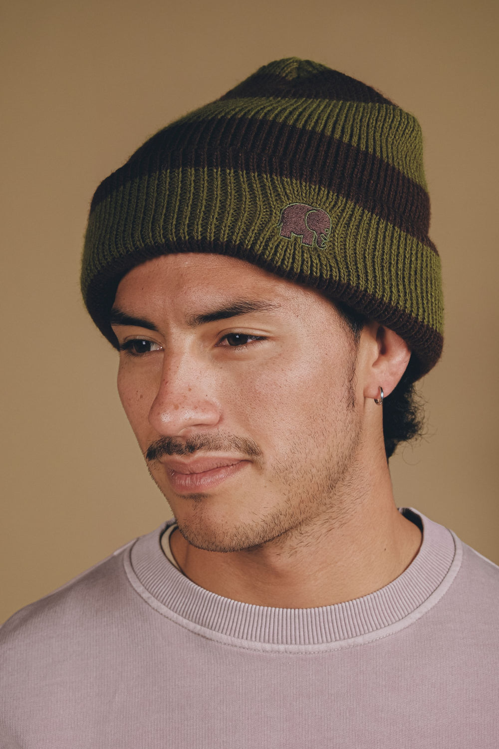 Persona che indossa il Montcabrer Beanie in Khaki/Coffee, con design a righe e dettaglio logo, in una foto ravvicinata. | TP_IMAGE_TYPE=MODEL_FRONT