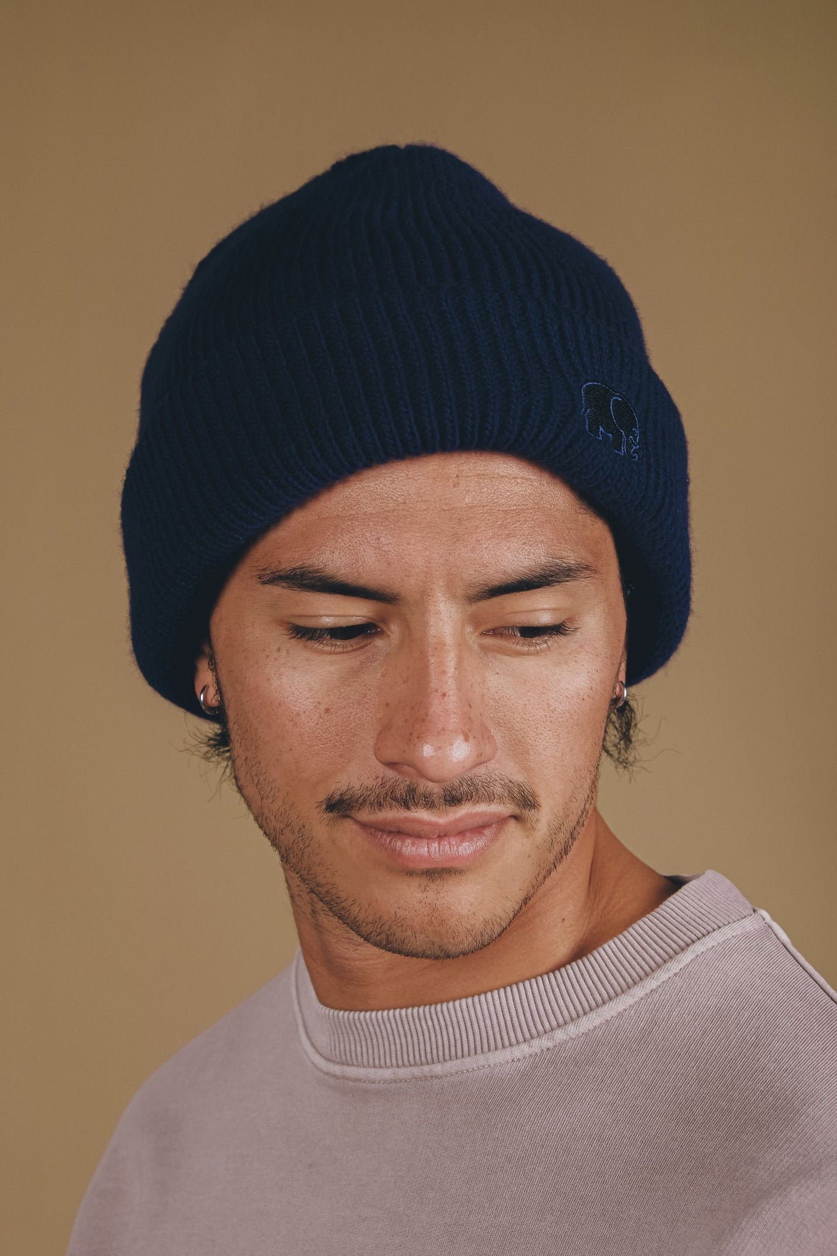 Personne portant un Campana Cuff Beanie en marine, regardant vers le bas avec un sourire doux, dans un style décontracté. | TP_IMAGE_TYPE=MODEL_FRONT