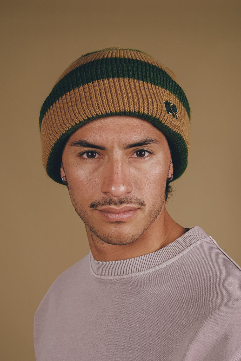 Personne portant le bonnet Montcabrer en Emmerald/Dune, avec des rayures de couleurs verte et beige, et un gros plan du visage sur un fond neutre. | TP_IMAGE_TYPE=MODEL_FRONT