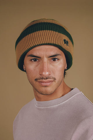 Personne portant le bonnet Montcabrer en Emmerald/Dune, avec des rayures de couleurs verte et beige, et un gros plan du visage sur un fond neutre. | TP_IMAGE_TYPE=MODEL_FRONT