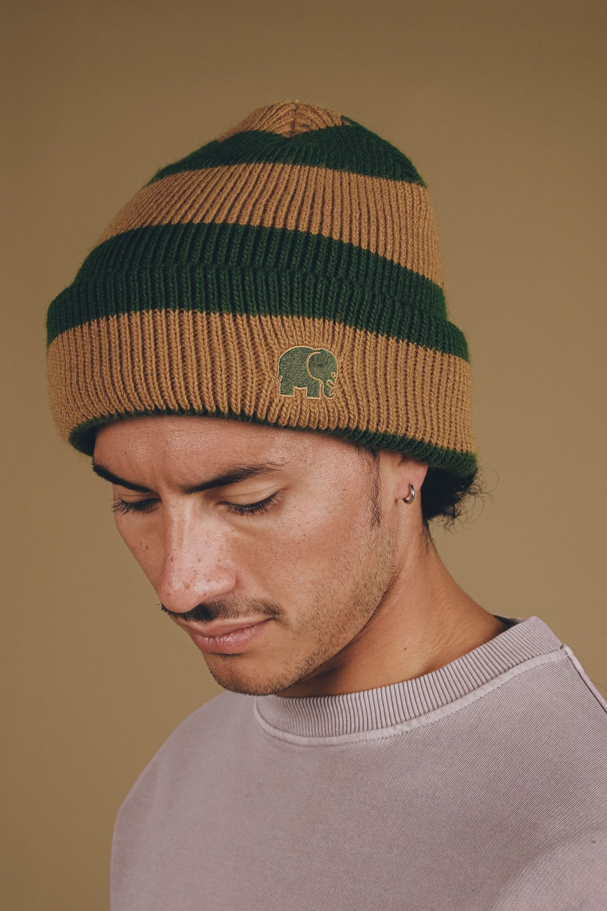 Personne portant le bonnet Montcabrer dans les coloris Emmerald et Dune, avec rayures horizontales et un logo éléphant brodé. | TP_IMAGE_TYPE=MODEL_FRONT