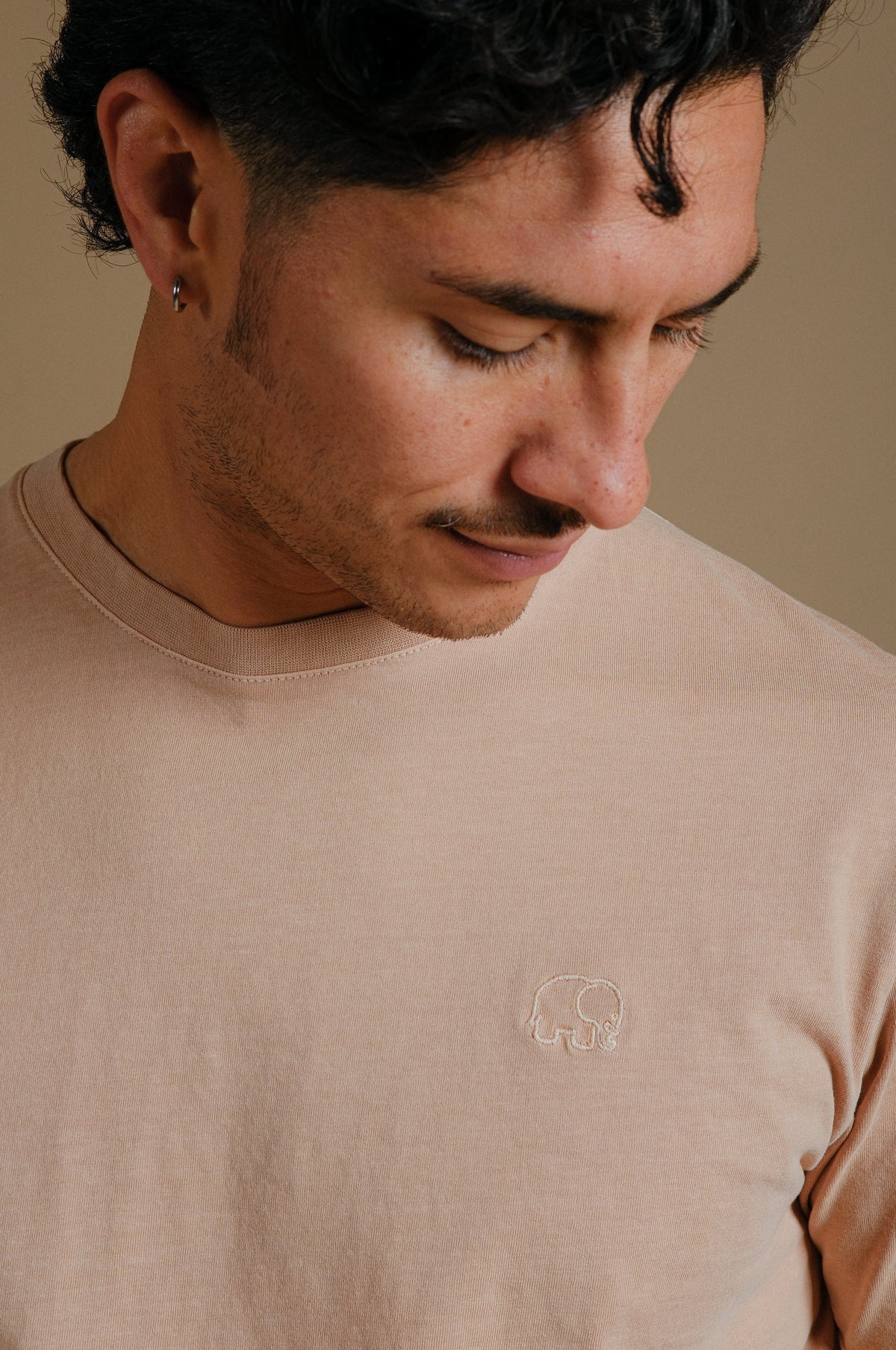 Personne portant un Essential Pigment T-Shirt en Cuban Sand, regardant vers le bas avec un logo brodé visible | TP_IMAGE_TYPE=MODEL_FRONT
