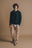 Persona che indossa un maglione in maglia verde pino abbinato a pantaloni beige chiaro e sneakers, in piedi su uno sfondo neutro. | TP_IMAGE_TYPE=MODEL_FRONT