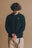 Persona che indossa un maglione Sella Knit verde pino con texture a coste, abbinato a pantaloni chiari, su uno sfondo neutro. | TP_IMAGE_TYPE=MODEL_FRONT