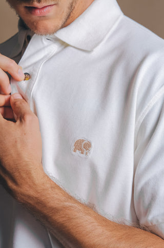 Persona che indossa la Alcalali Pigment Dyed Organic Polo Shirt nel colore Almond Milk, con un delicato ricamo a forma di elefante e vista ravvicinata dei bottoni | TP_IMAGE_TYPE=MODEL_FRONT