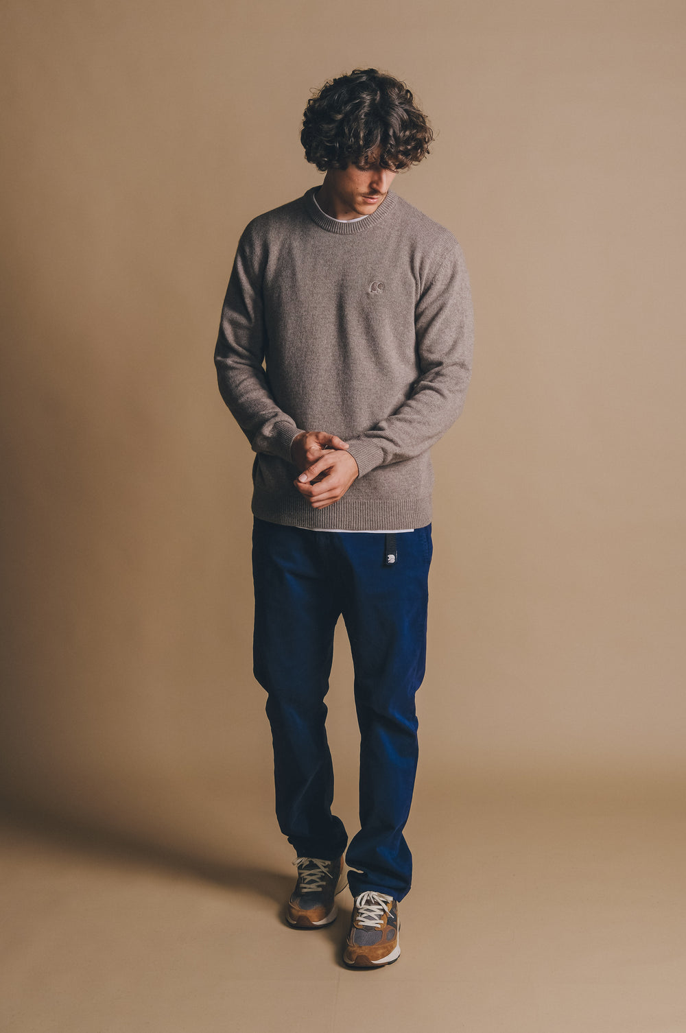 Person wearing the Tarbena Knit Stone sweater styled with blue pants, standing with hands clasped in front of a neutral background. | TP_IMAGE_TYPE=MODEL_FRONT