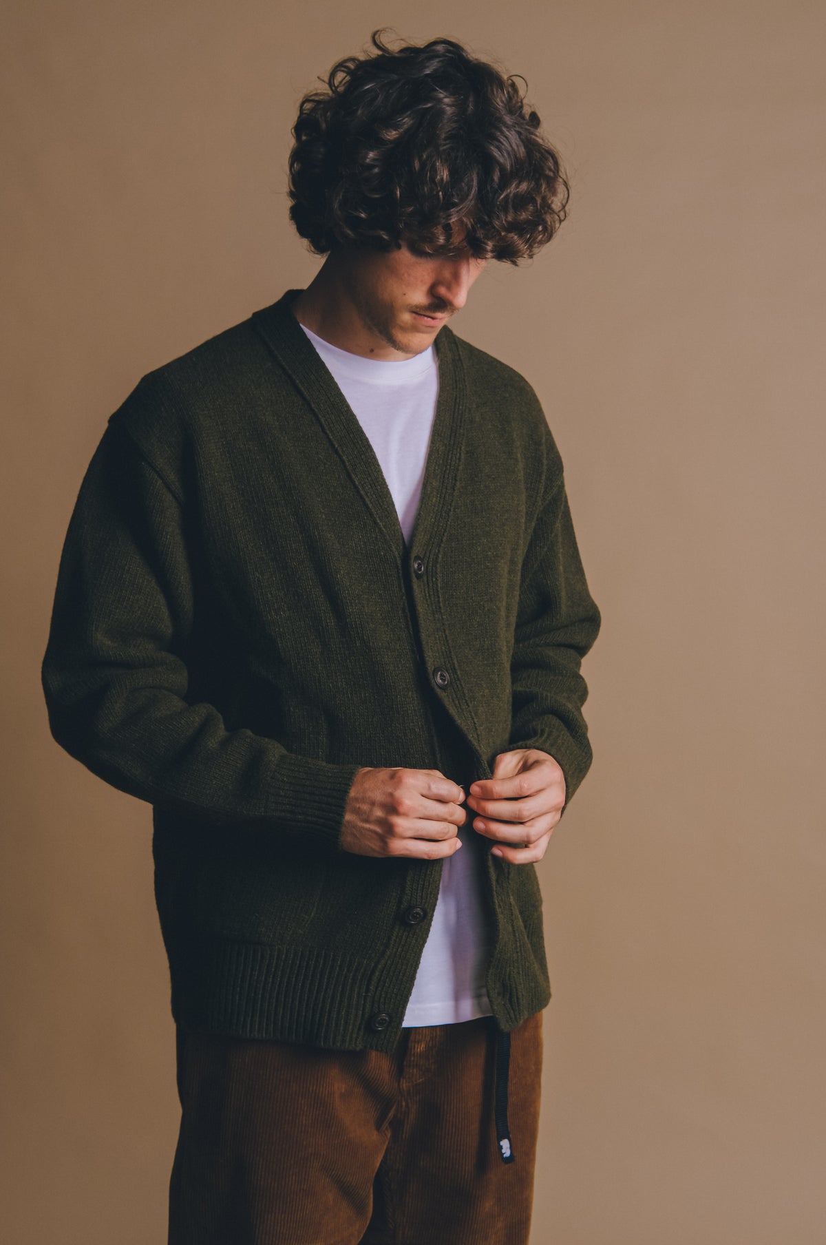Personne portant le cardigan Relleu en Ivy Green, boutonnant le devant tout en regardant vers le bas | TP_IMAGE_TYPE=MODEL_FRONT