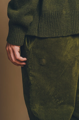 Persona che indossa pantaloni in velluto a coste verde oliva con vista su un cardigan in maglia verde oliva.